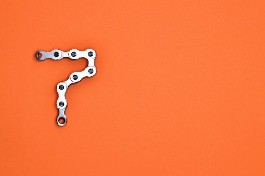 Artistic arrangement of bicycle chain shaped like number seven on orange background.