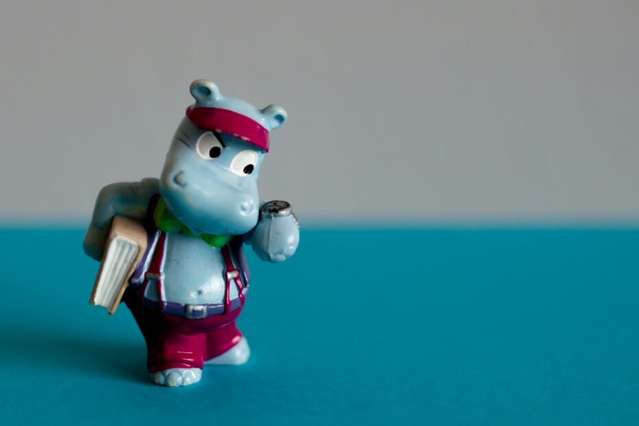 A small toy hippo holding a book on a table